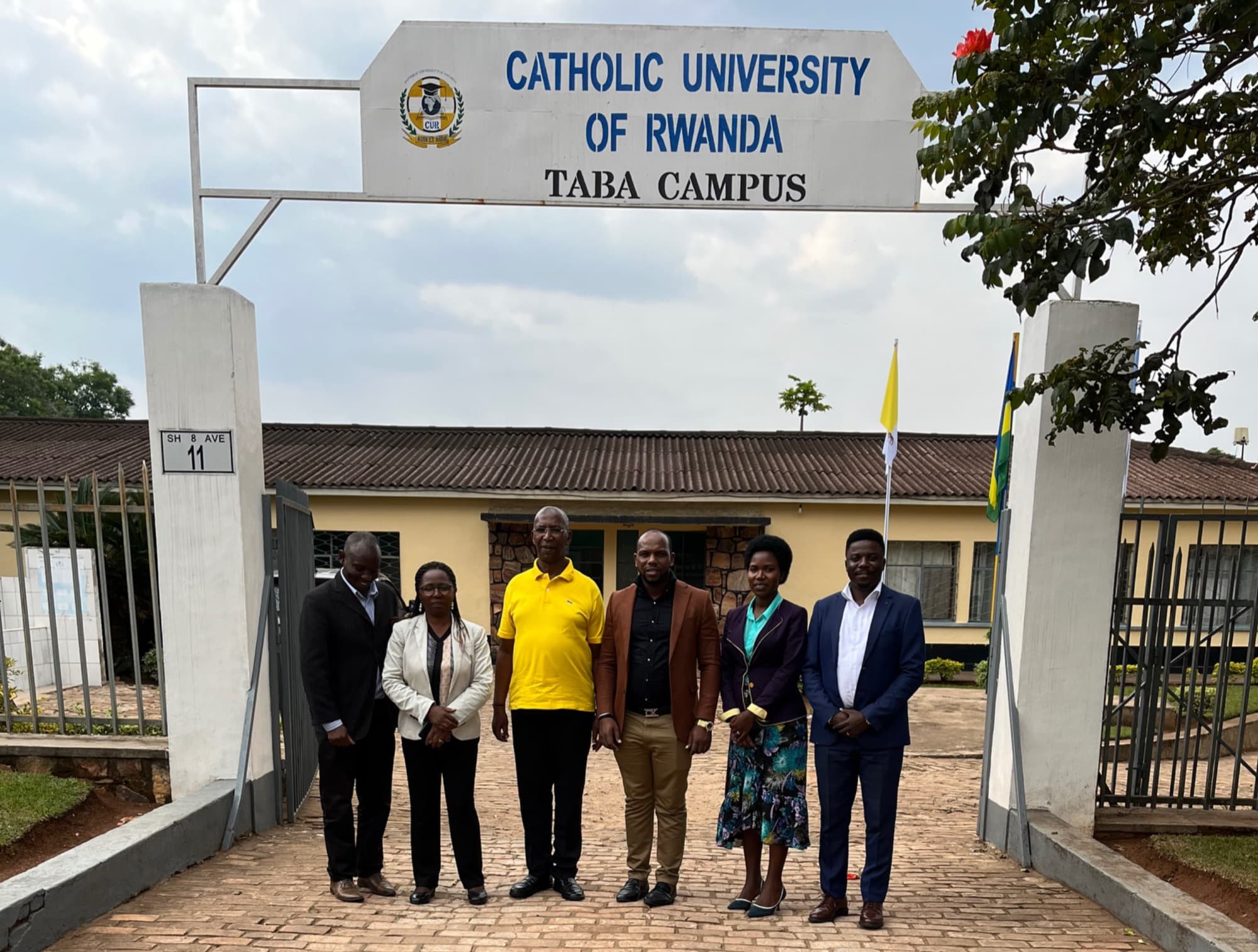 Six people standing under the entrance arch of the Catholic University of Rwanda, Taba Campus, after signing a memorandum of understanding.